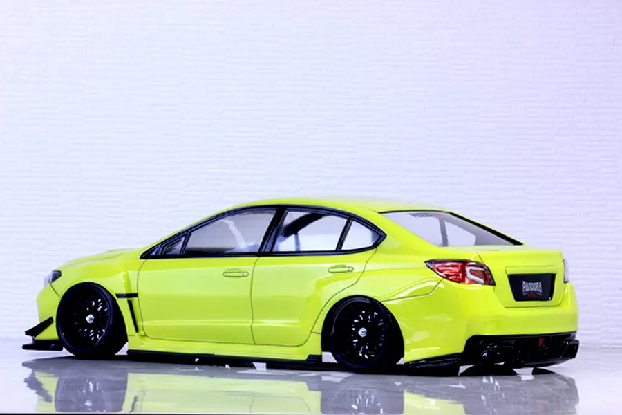 Side-rear view of a painted bright yellow RC drift car body shell mounted on a chassis with black wheels against a white wall.