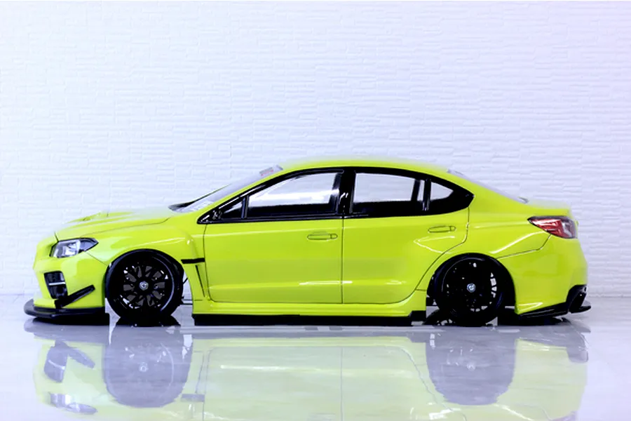 Side profile of a bright yellow RC drift car body shell mounted on a chassis with black multi-spoke wheels against a light background.