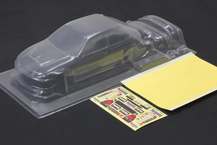 Unpainted clear polycarbonate RC car body shell with a decal sheet and mask sheet on a dark background.