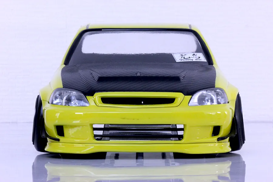 Front view of a yellow RC car body shell featuring a black carbon-fiber-style hood and front bumper details on a white background.