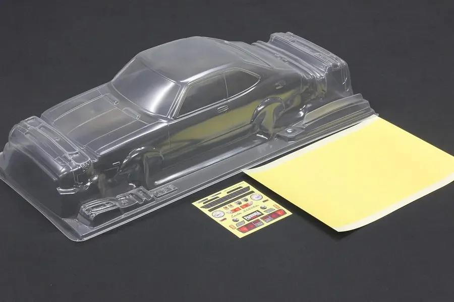Unpainted clear polycarbonate RC car body shell with a mask sheet and decal sheet on a dark surface.