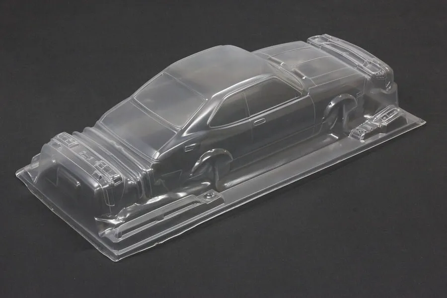 Unpainted clear polycarbonate RC car body shell on a dark grey surface, viewed from a high angle.
