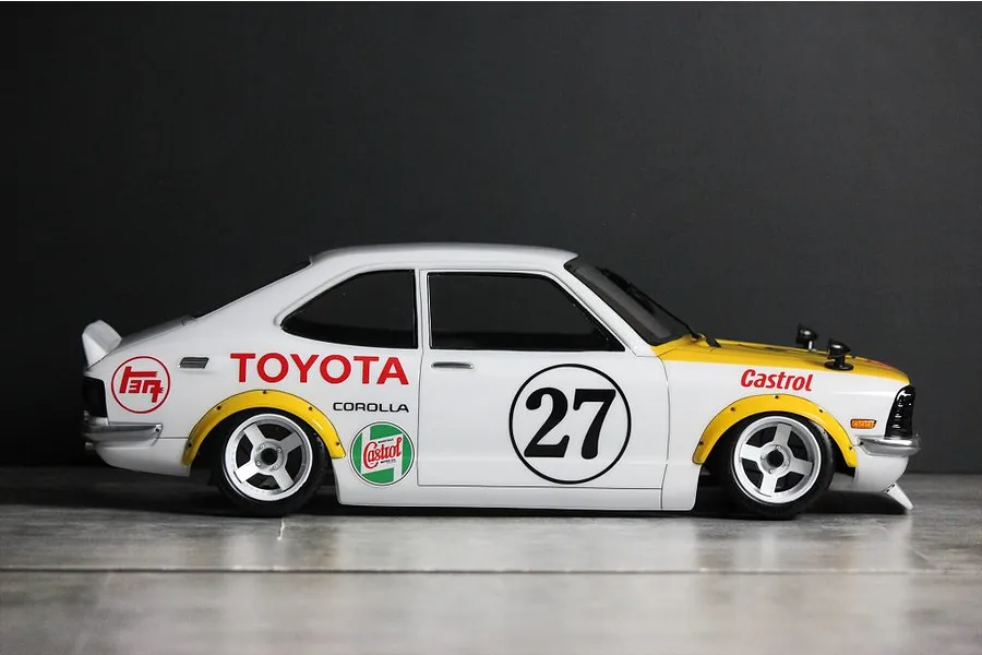 Side profile of a painted Toyota Corolla Levin TE27 RC body shell with racing liveries, number 27, and white wheels on a grey surface.
