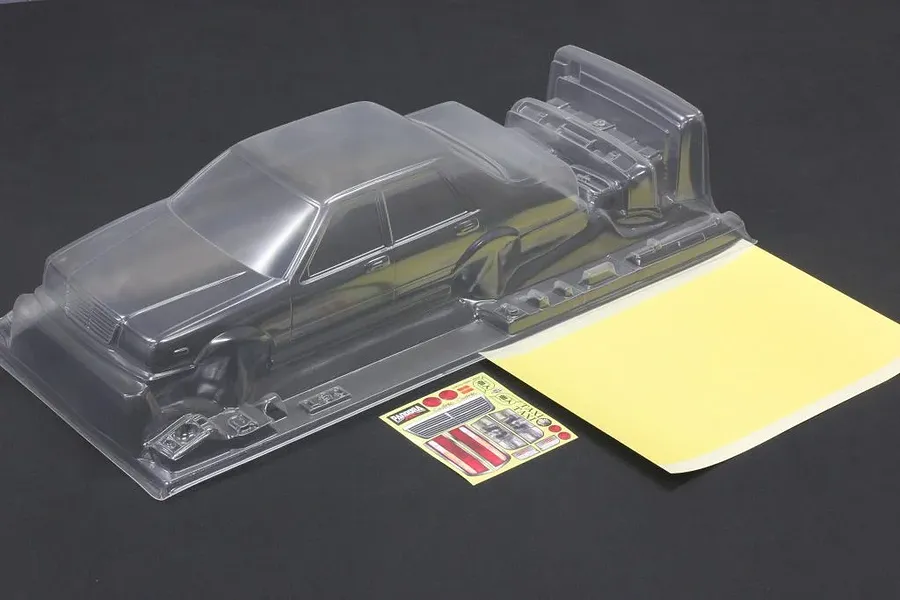 Unpainted clear polycarbonate RC car body shell with accessories sheet and masking stickers on dark surface.