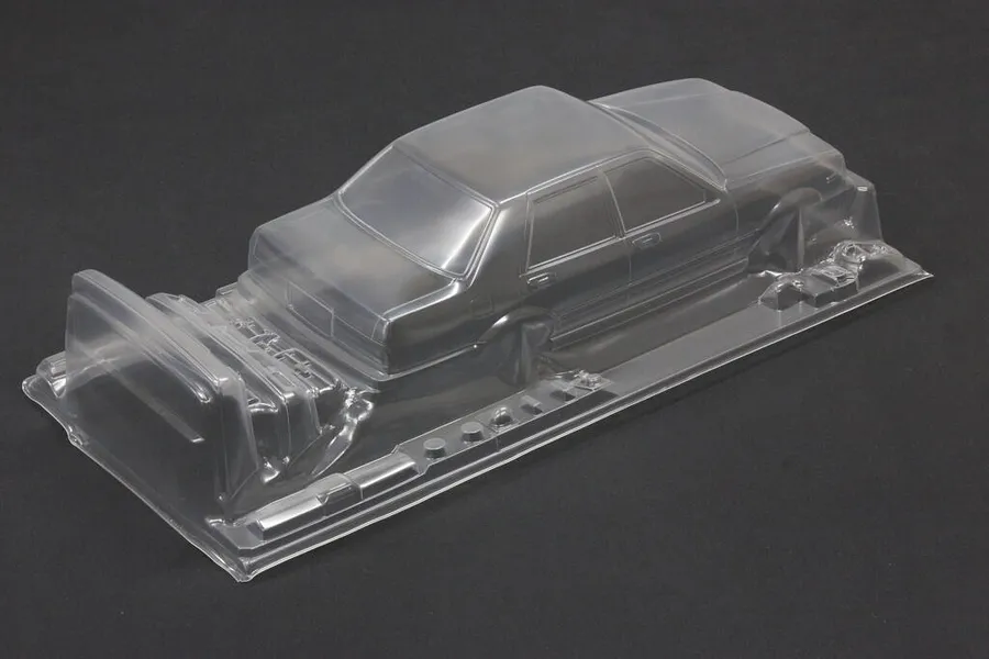 Unpainted clear polycarbonate RC sedan body shell on a dark surface, showing front and side profile details.