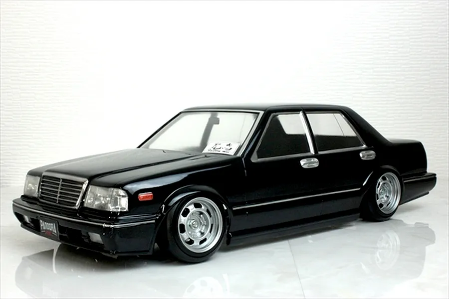 A black RC drift car body shell styled as a classic sedan on a white reflective surface.