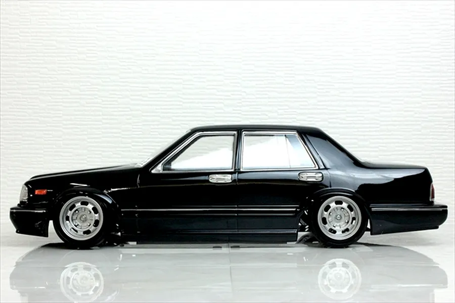 Side profile view of a black RC drift car body shell mounted on a chassis with custom silver wheels, set against a white textured background.