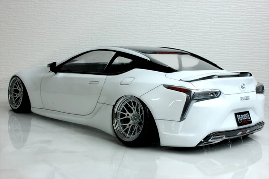 Rear three-quarter view of a white Pandora RC Lexus LC drift body shell on a glossy white surface with a brick textured background.