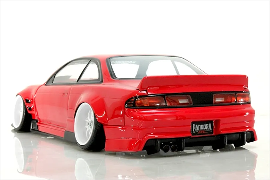 Rear three-quarter view of a painted red RC drift car body shell, featuring a rear spoiler, wide body kit, deep dish white wheels, and dual exhaust pipes on a white studio background.