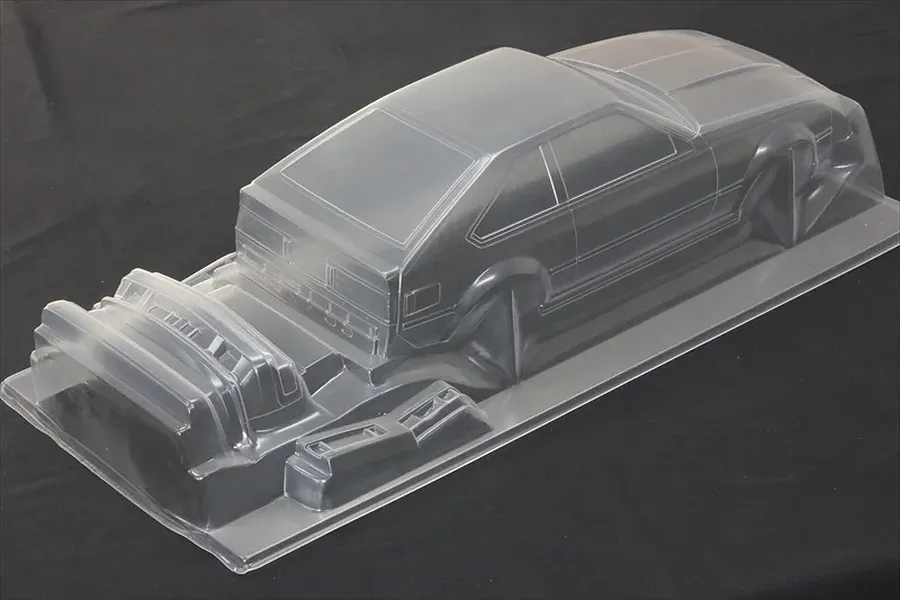 Unpainted clear polycarbonate RC car body shell of a Toyota Celica XX A60 on a dark surface.