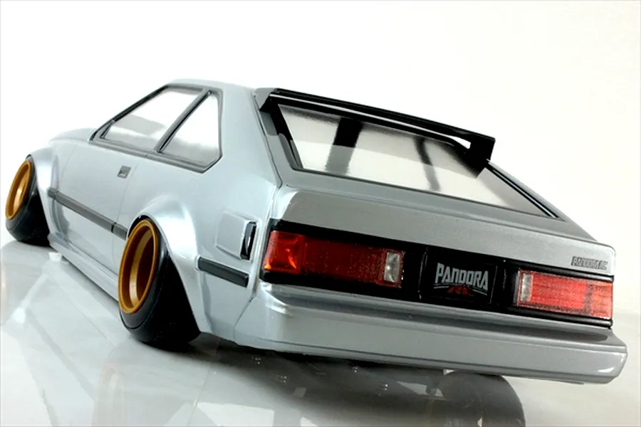 Rear three-quarter view of a silver Toyota Celica XX RC drift car body shell with gold deep dish wheels and black trim against a white background.