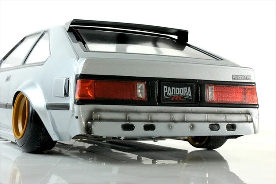 Rear-three-quarter view of Pandora RC Toyota Celica XX A60 RC body shell in silver with custom weathering, roof spoiler, and gold wheels.