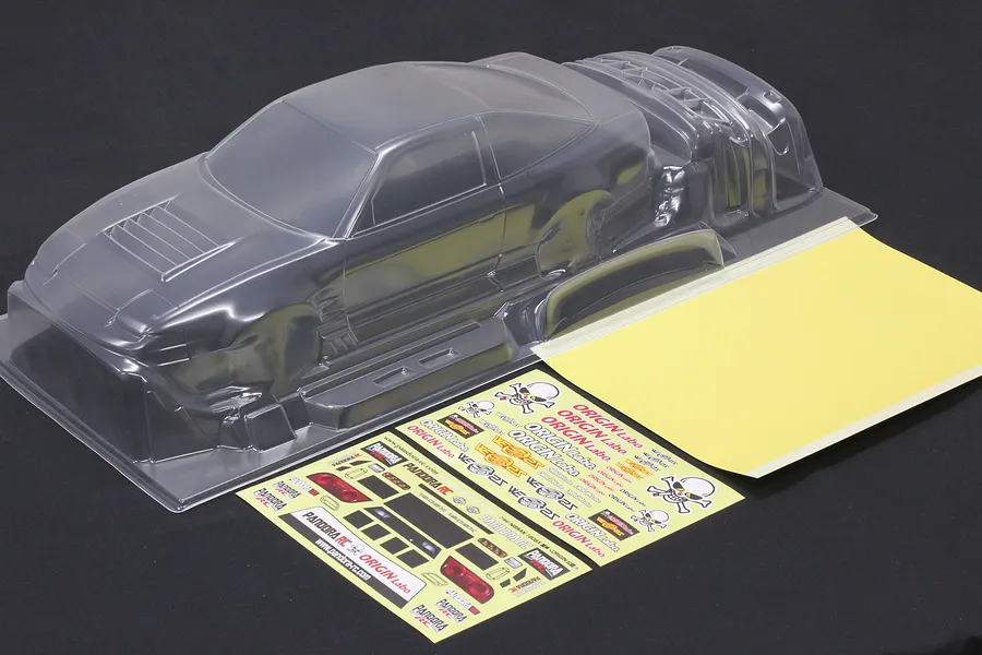 Unpainted clear polycarbonate RC drift car body shell with window masks and decal sheet on a dark background.