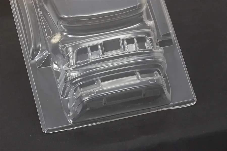 Unpainted clear polycarbonate RC car body shell showing front bumper and accessories molded into the sheet.