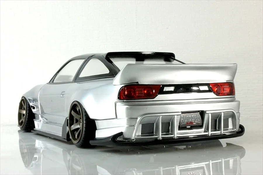 Rear quarter view of a silver RC drift car body shell, featuring a large rear wing, detailed taillights, and wide wheels against a white background.