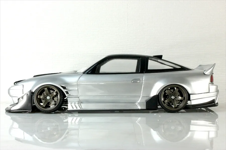 Side profile view of a silver and black RC drift car body shell on a reflective surface against a white background.