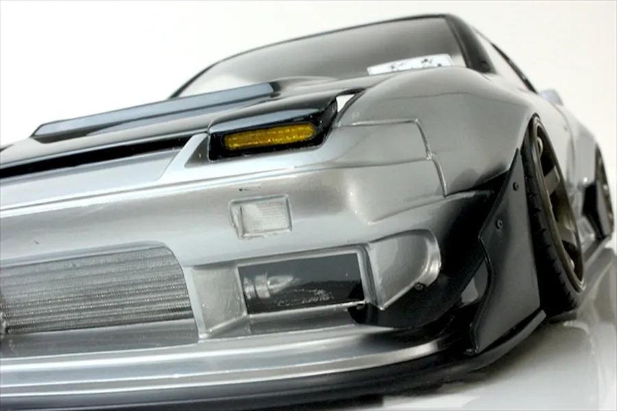 Close-up low-angle view of the front bumper, pop-up headlight, and intercooler on a silver Pandora RC 180SX body shell.