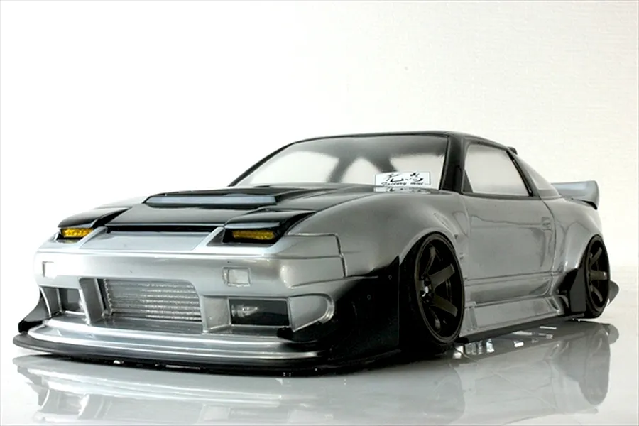 Low angle front three-quarter view of a silver and black Pandora RC RPS13 180SX drift car body shell with custom aero kit and wheels on a reflective white surface.