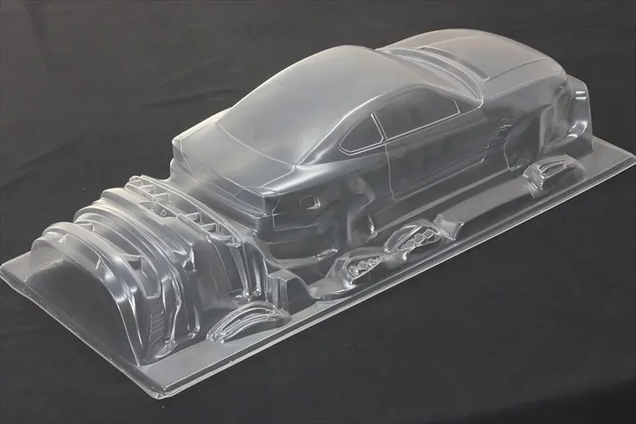 Unpainted clear polycarbonate RC drift car body shell with additional molded parts on a dark background.