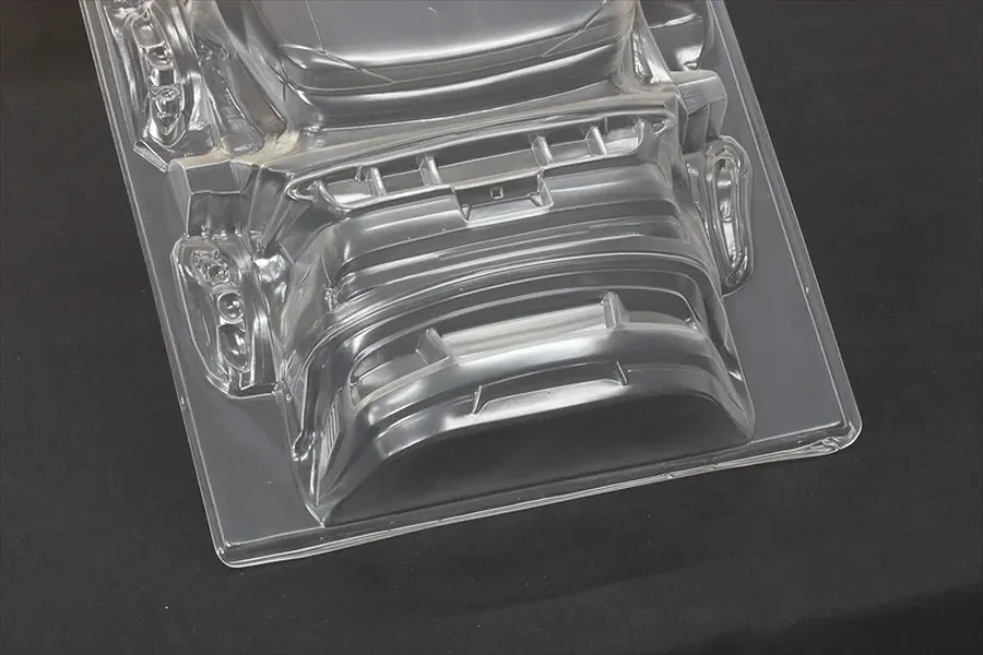 Unpainted clear polycarbonate RC car body shell parts molded on a sheet, set against a dark background.