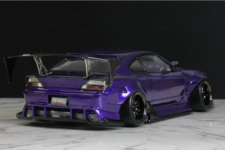 Rear three-quarter view of a purple painted RC drift car body shell mounted on a chassis with a large rear wing and black wheels.