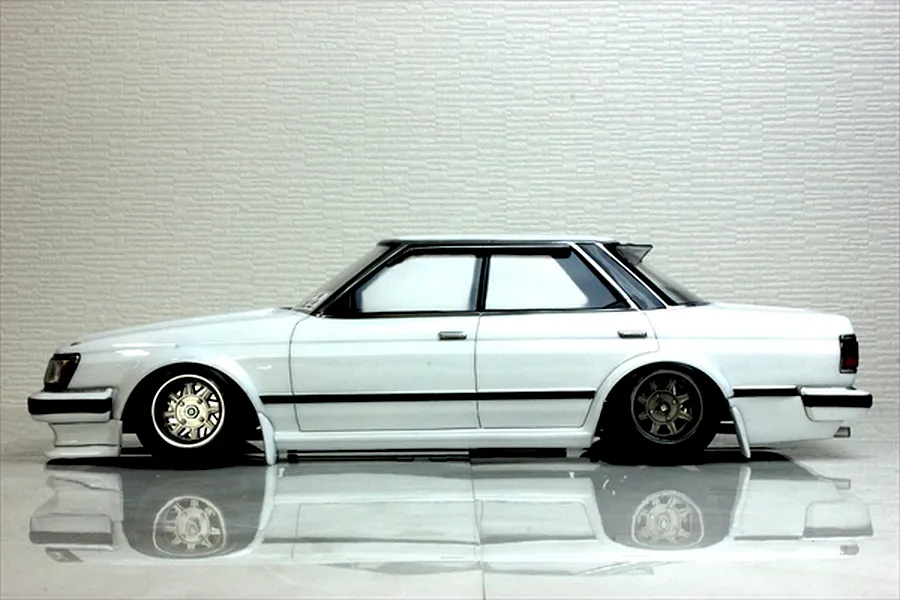Side profile view of a white RC drift car body shell styled after a classic Toyota Mark 2 GX71 on a reflective surface.