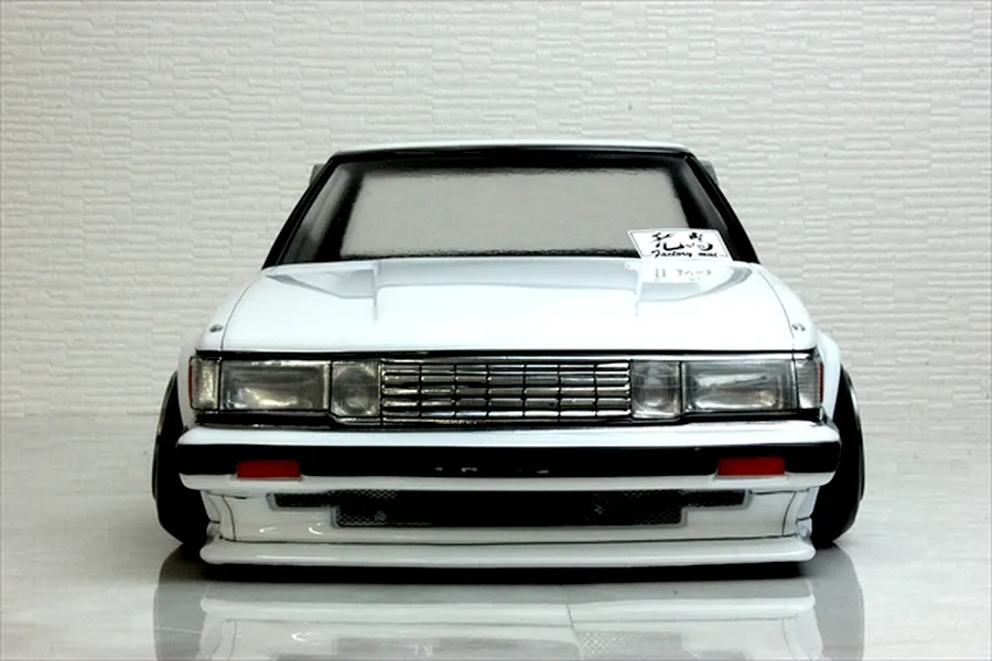 Front view of a white RC drift car body shell, showing detailed grille, headlights, and a sticker on the windshield against a neutral background.
