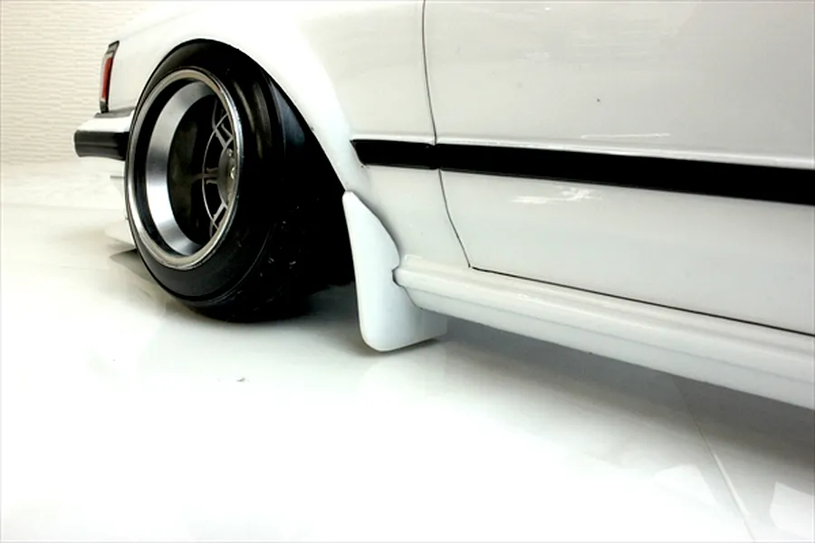 Close-up of the front wheel and side body panel of a white RC drift car model showcasing deep dish wheel and mudflap.