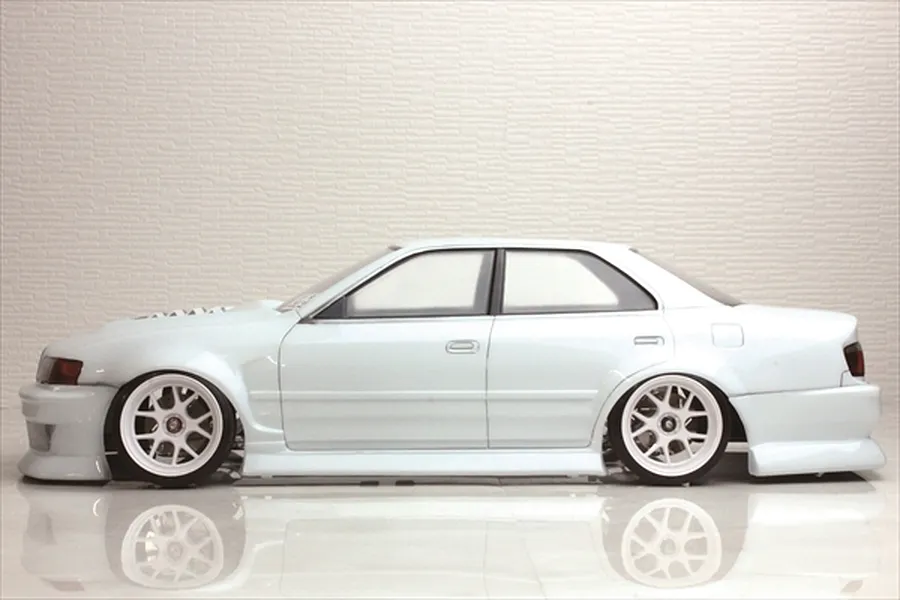 Side profile view of a white Toyota Chaser JZX100 RC drift car body shell on a reflective white surface with a textured white background.