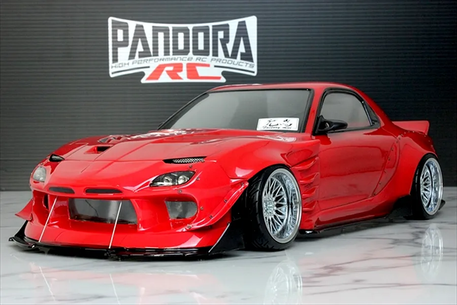 Red RC drift car body shell of a Mazda RX-7 FD3S with wide body kit and chrome mesh wheels displayed indoors.
