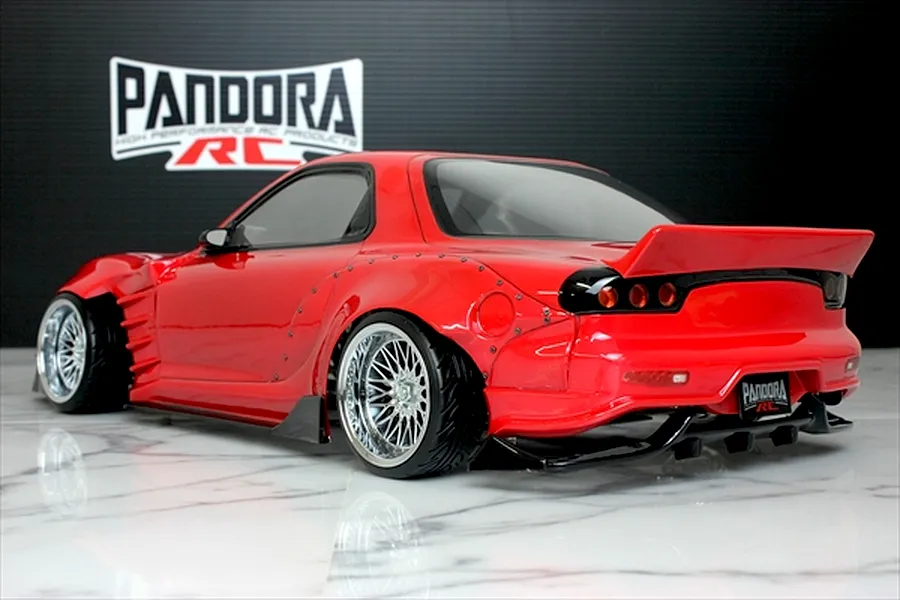 Rear-three-quarter view of a painted red Mazda RX-7 FD3S RC drift car body with widebody fenders and chrome mesh wheels.