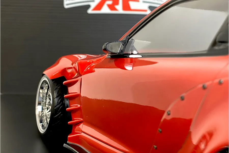Close-up of a red RC drift car body side profile, highlighting the front fender aero vents, wheel, and mirror.
