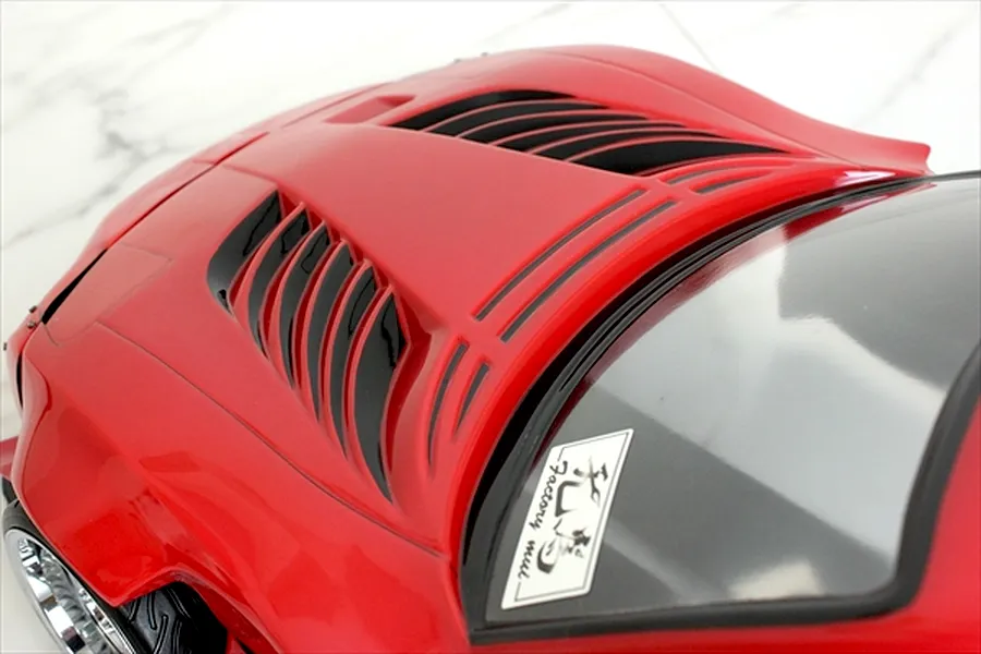 Close-up of the red RC car body bonnet featuring black vents and a windshield sticker against a white marble background.