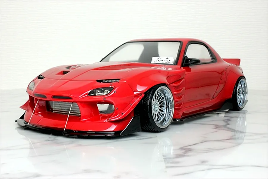 Red RC drift car body shell mounted on a chassis with custom wide body kit and chrome deep dish wheels.