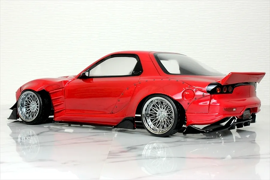 Rear-three-quarter studio shot of a red Mazda RX-7 RC drift car body with wide body kit and chrome mesh wheels.