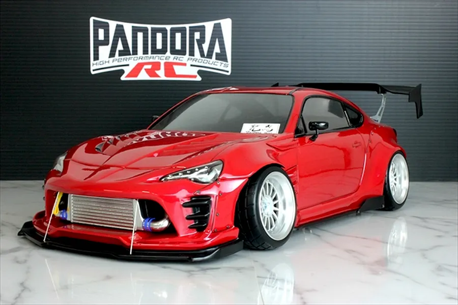 Red Pandora RC Toyota 86 body shell with wide body kit, large rear wing, and intercooler displayed on a marble surface.