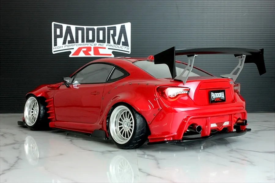 Rear-three-quarter view of a painted red Toyota 86 RC drift car body shell with a large rear wing, widebody fenders, and Pandora RC logo backdrop.