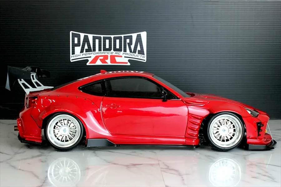 Side profile of a red Toyota 86 RC drift car body with wide fenders, large rear wing, and silver mesh wheels.