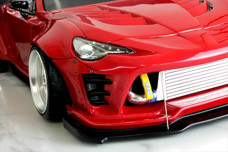 Close-up front quarter view of a red RC drift car body showing the front bumper, intercooler, and wide-body fender.