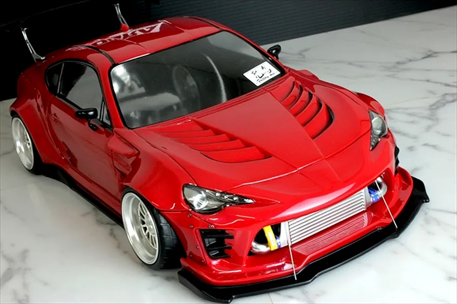 High angle shot of a custom red Pandora RC Toyota 86 body shell with widebody kit and intercooler on a marble surface.