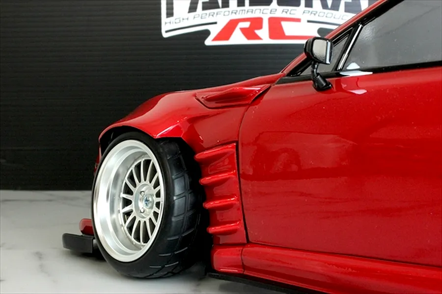 Close-up of the front wheel arch and fender of a red radio-controlled drift car body with wide body kit and deep dish wheel.