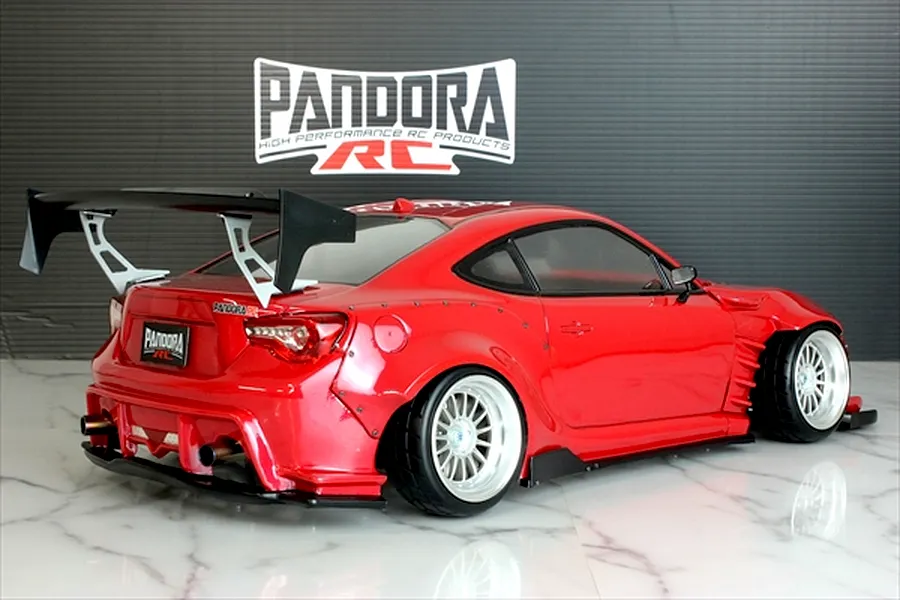 Rear-three-quarter view of a painted red Toyota 86 RC drift car body with widebody kit and large rear wing.
