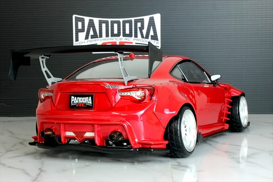 Rear view of a red RC drift car with a large black wing, wide body kit, and Pandora RC logo in the background.