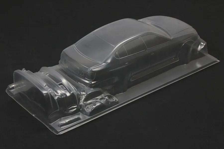 Unpainted clear polycarbonate RC car body shell with additional bumper parts on a dark background.