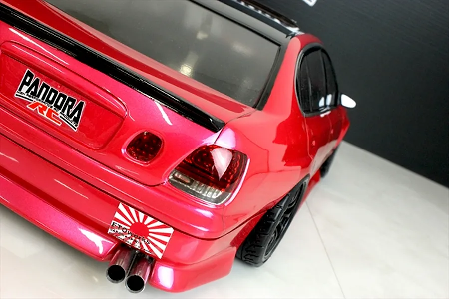 Rear three-quarter view of a painted pink RC drift car body shell showing tail lights, twin exhaust pipes, and sponsor decals.
