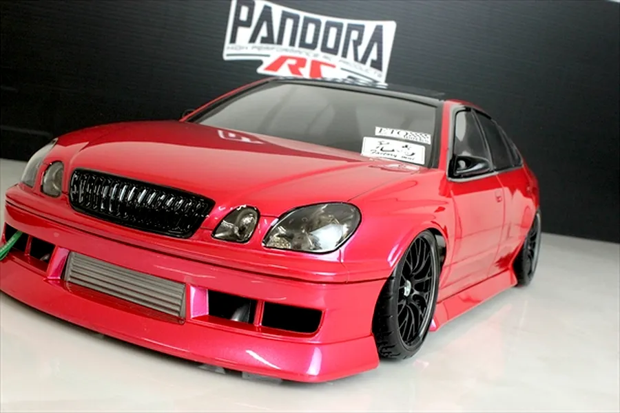 Red RC drift car body shell of a Toyota Aristo JZS161 on a reflective white surface with a Pandora RC logo backdrop.