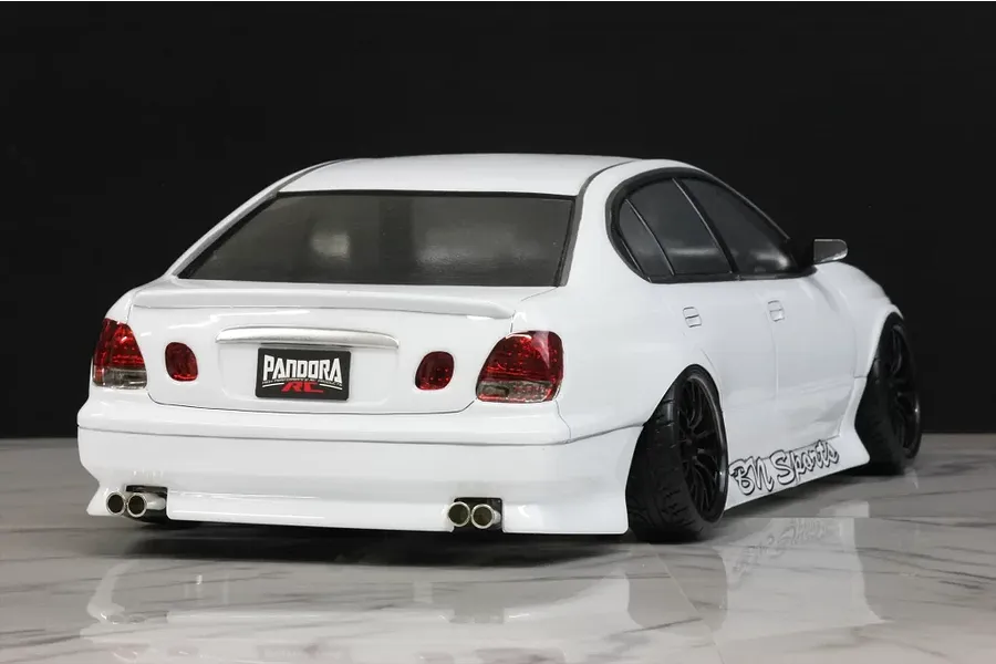 Rear-three-quarter view of a white RC drift car body shell, featuring dual exhaust tips, BN Sports side graphics, and black wheels on a reflective surface.