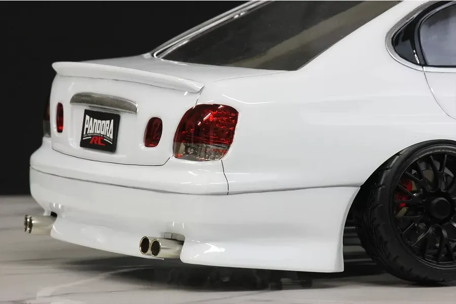 Close-up of the rear section of a white RC drift car body shell, showing tail lights, twin exhaust tips, rear spoiler, and black wheel.