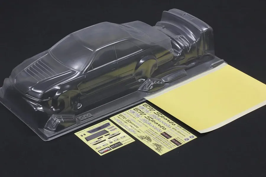Unpainted clear polycarbonate RC car body shell with window masks and decal sheets on a dark background.