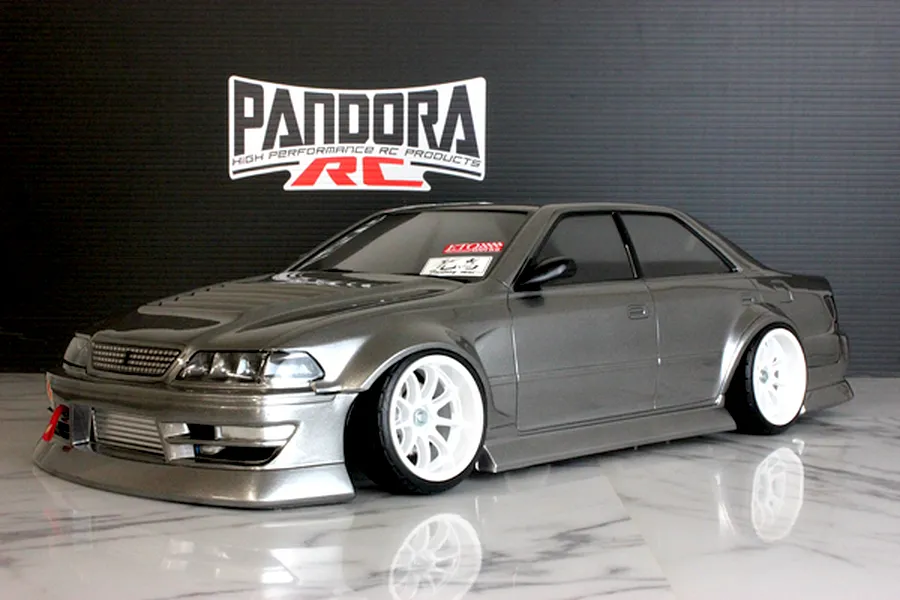 Studio photo of a grey Toyota Mark II JZX100 RC drift car body shell on a white marble surface with a Pandora RC logo backdrop.